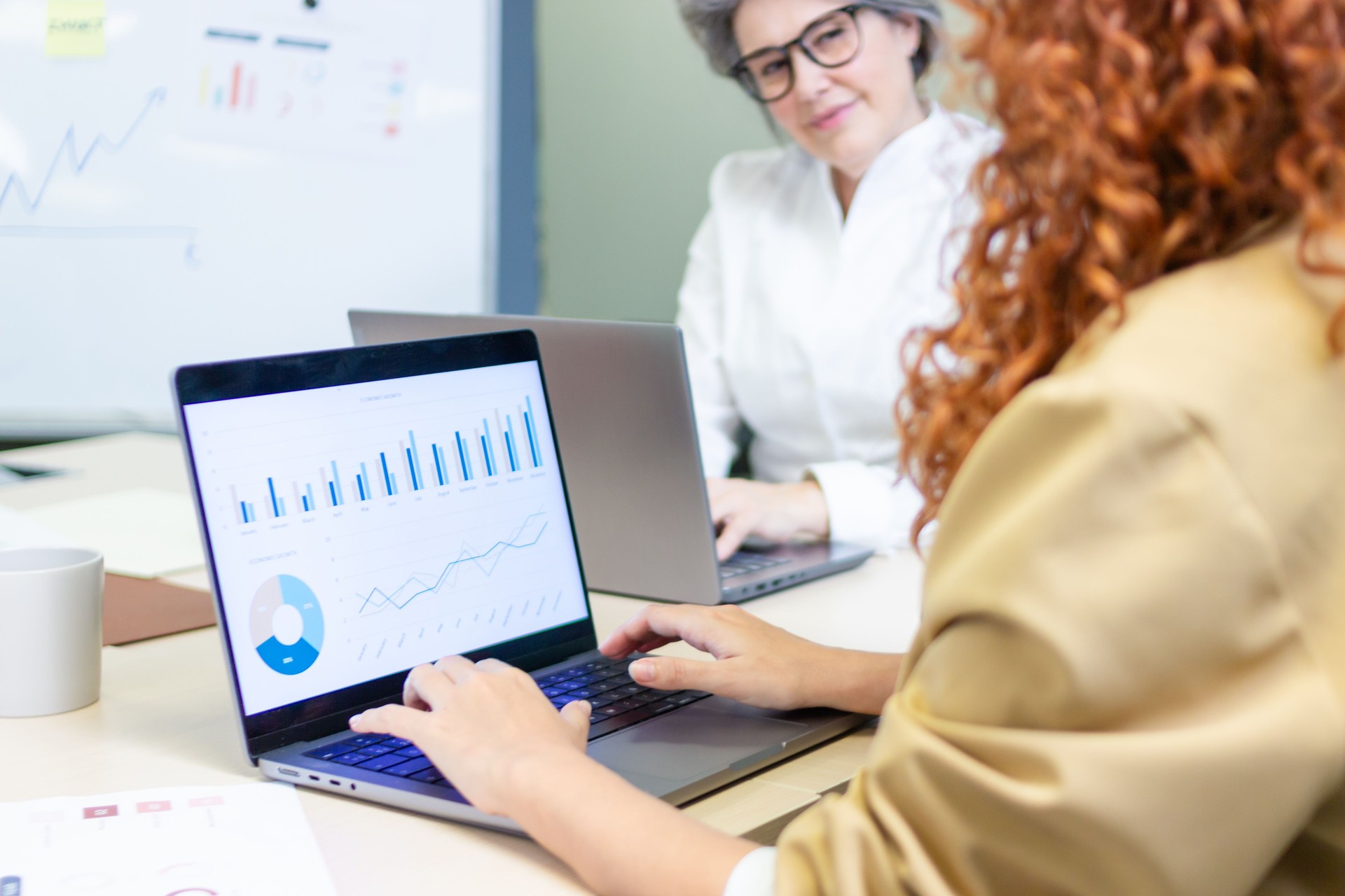 Coworkers analyzing charts on laptops in office meeting